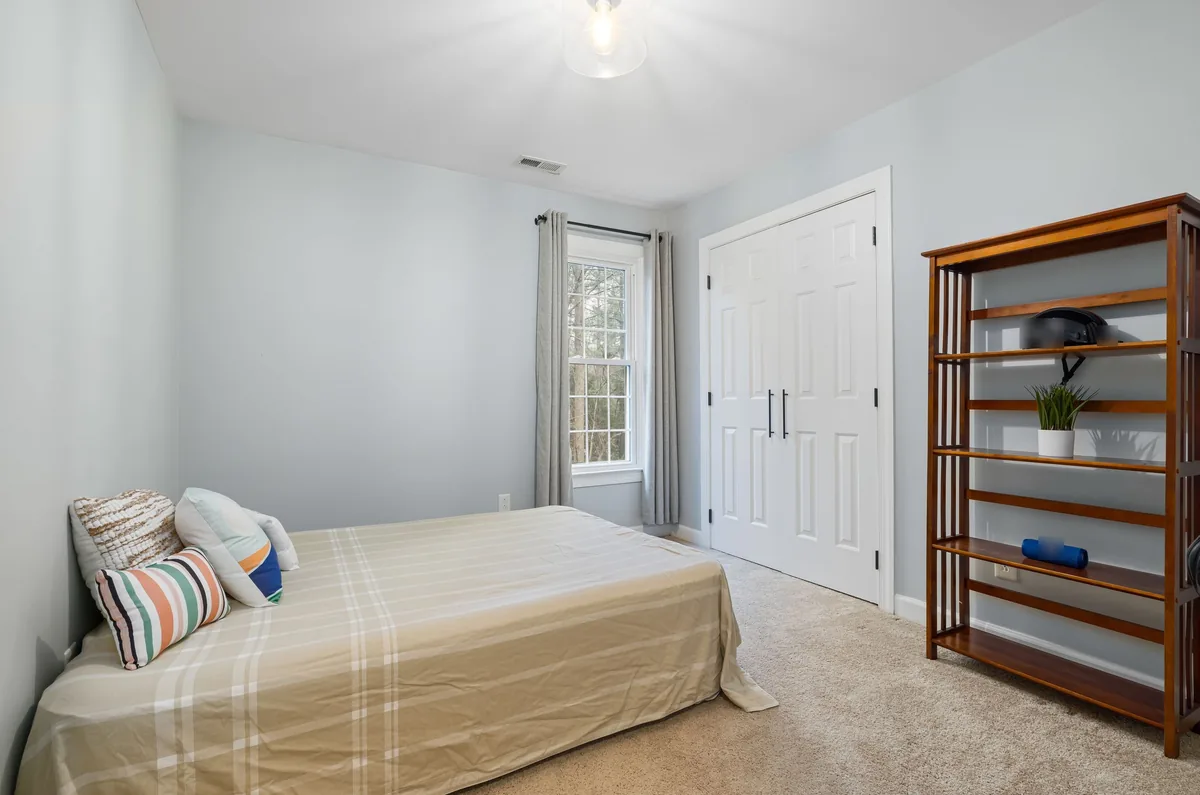Small bedroom with blue-grey walls, beige carpet, white closet doors and a wooden bookshelf before AI redesign