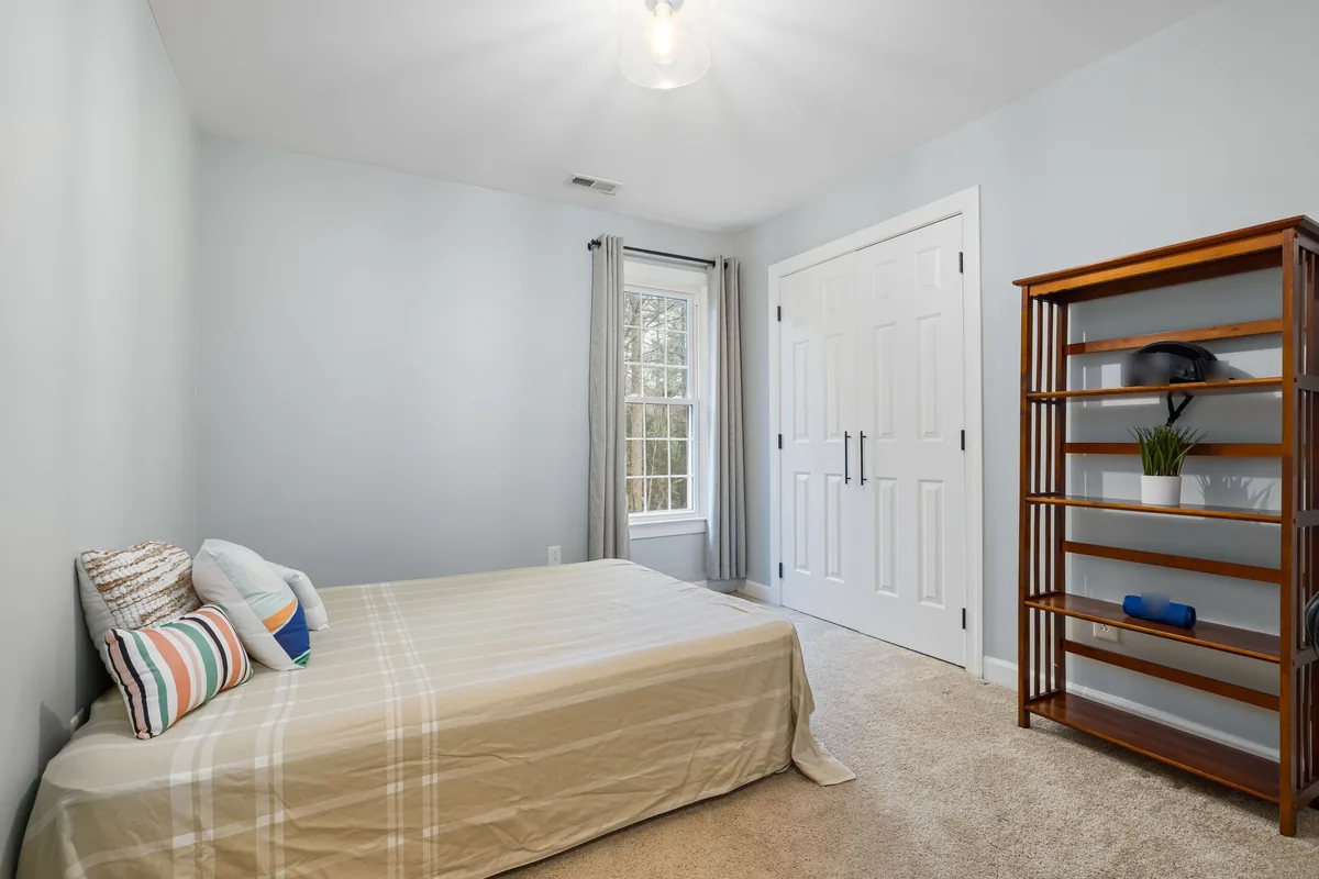 Small bedroom with blue-grey walls, beige carpet, white closet doors and a wooden bookshelf before AI redesign
