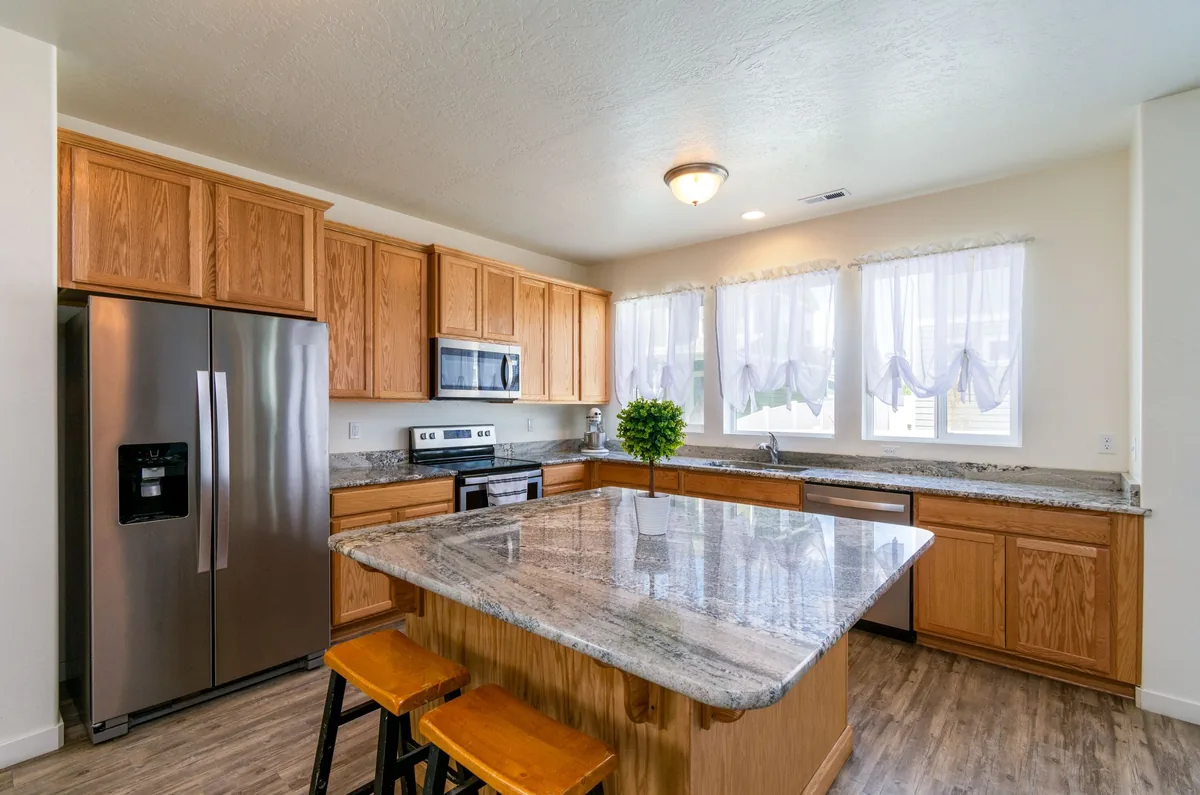 Dated kitchen with oak cabinets, granite island, stainless fridge and three curtained windows before AI redesign
