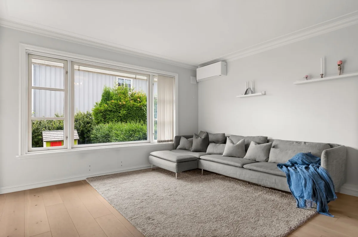 Plain living room with a grey sectional sofa, shaggy rug and large garden window before AI redesign